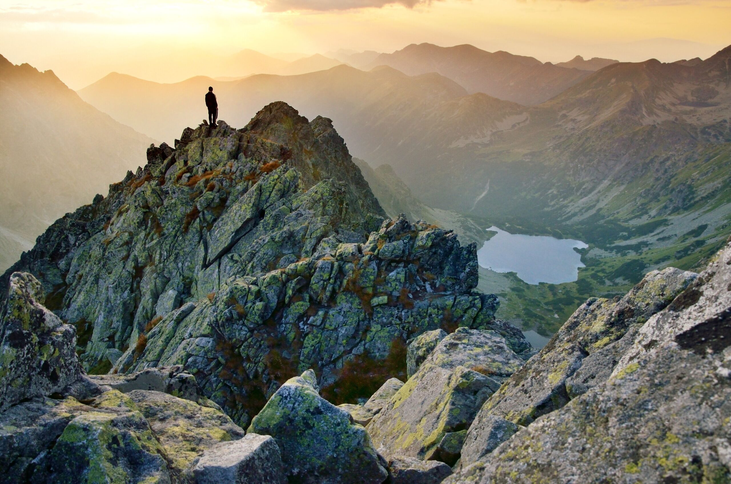 Mann steht im Gebirge auf einem Gipfelgrat.