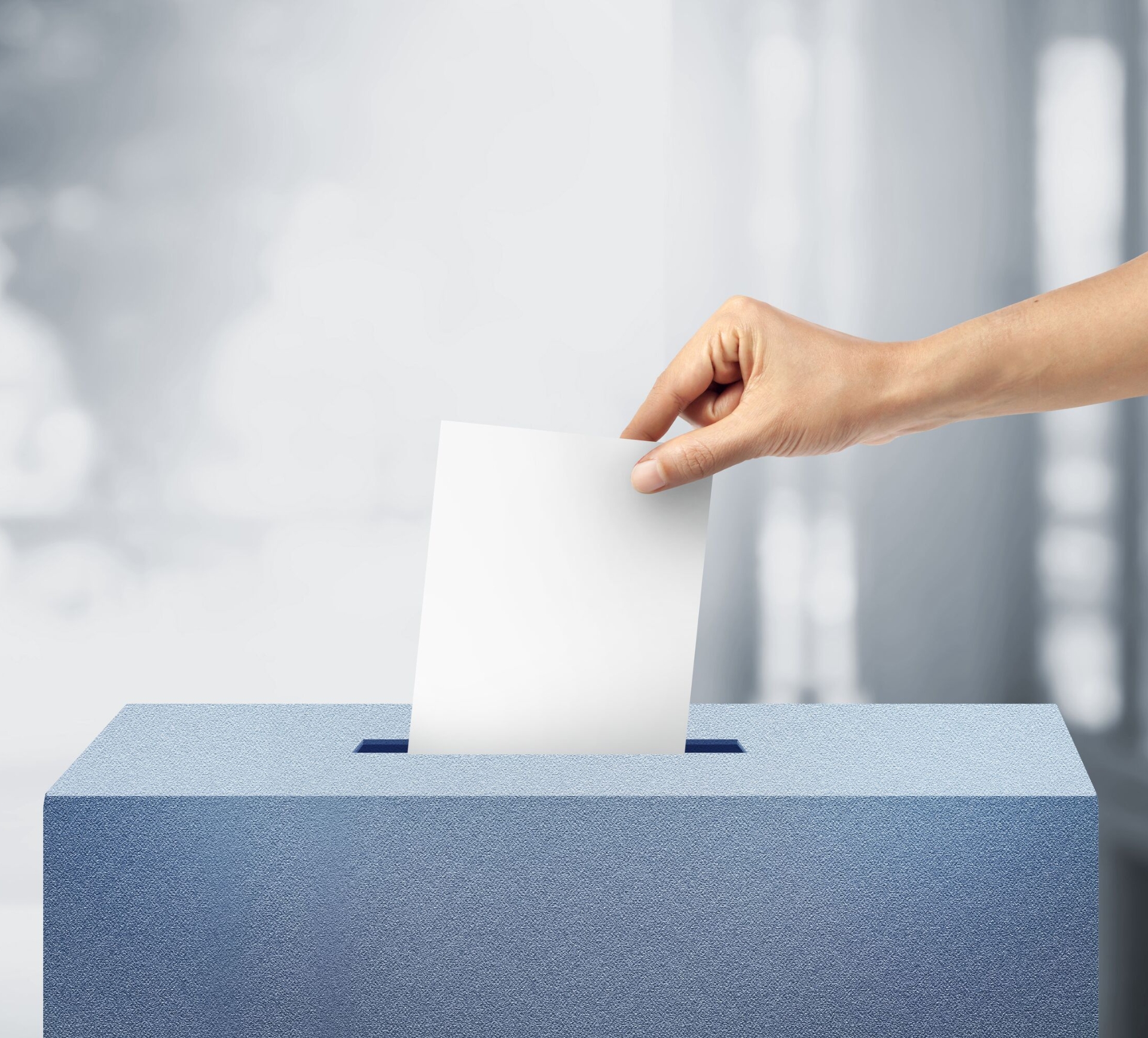 Hand mit Stimmzettel an an der Wahlurne